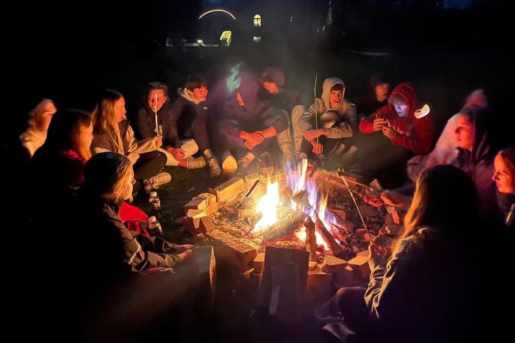 Young people seated around a fire at night.